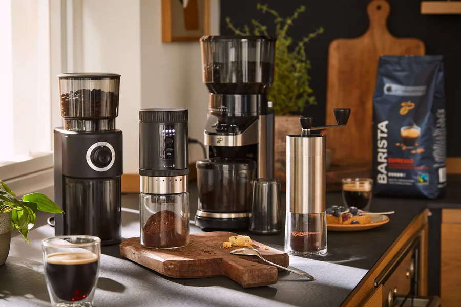 Čtyři mlýnky na kávu a balíček zrnkové kávy jsou uspořádány na kuchyňské lince s kávou a zákuskem.