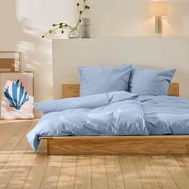 Postel s modrým povlečením stojí na dřevěné podlaze. Za postelí jsou dva obrazy.