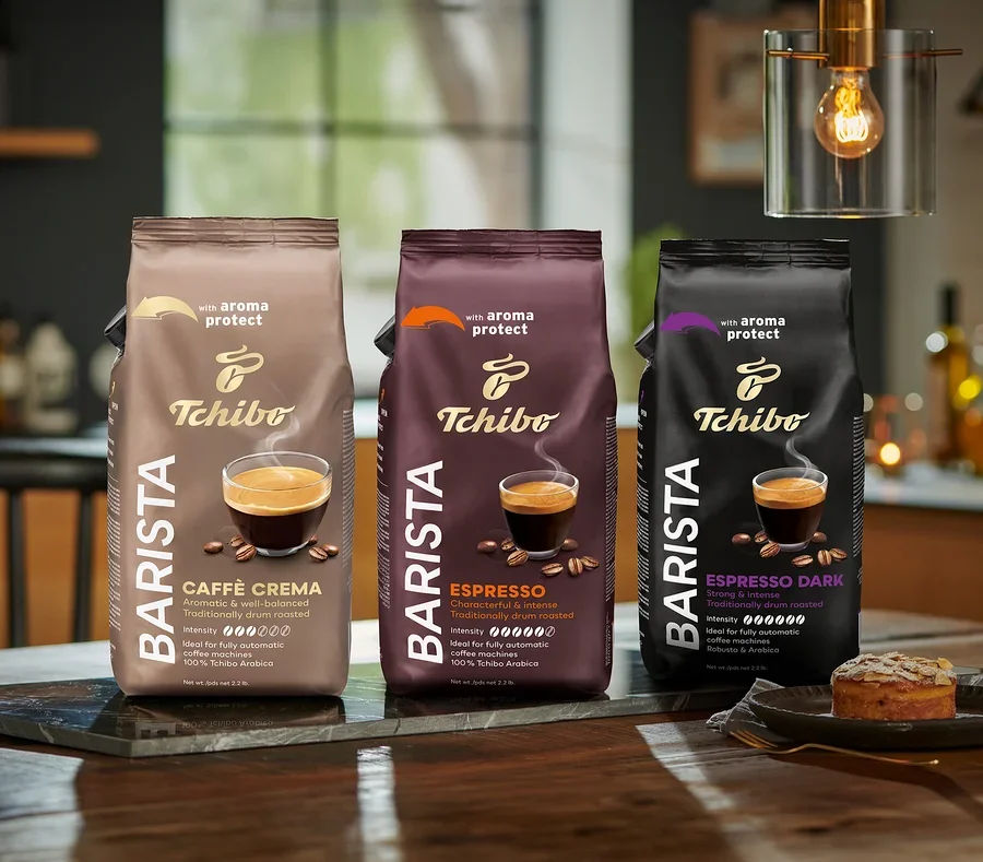Tři balení zrnkové kávy Tchibo Barista stojí na stole, zleva doprava: Caffè Crema, Espresso a Espresso Dark.