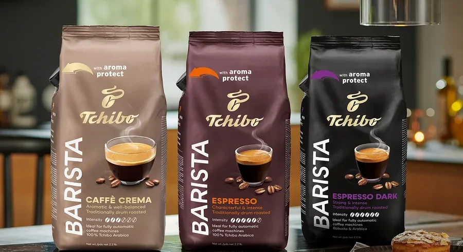 Tři balení zrnkové kávy Tchibo Barista stojí na stole, zleva doprava: Caffè Crema, Espresso a Espresso Dark.