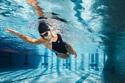 Žena plave pod vodou v bazénu v černých plavkách arena Feel Lily Swim Pro Back.