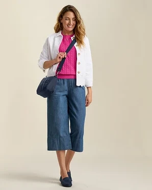 Žena v džínových culottes, růžovém svetru a džínové bundě s anglickou krajkou. Modrá taška přes rameno a ladící nazouváky.