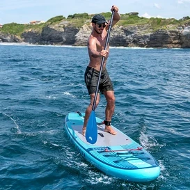 Muž pádluje na modrém paddleboardu Aqua Marina »Beast« 10'6“ na moři.