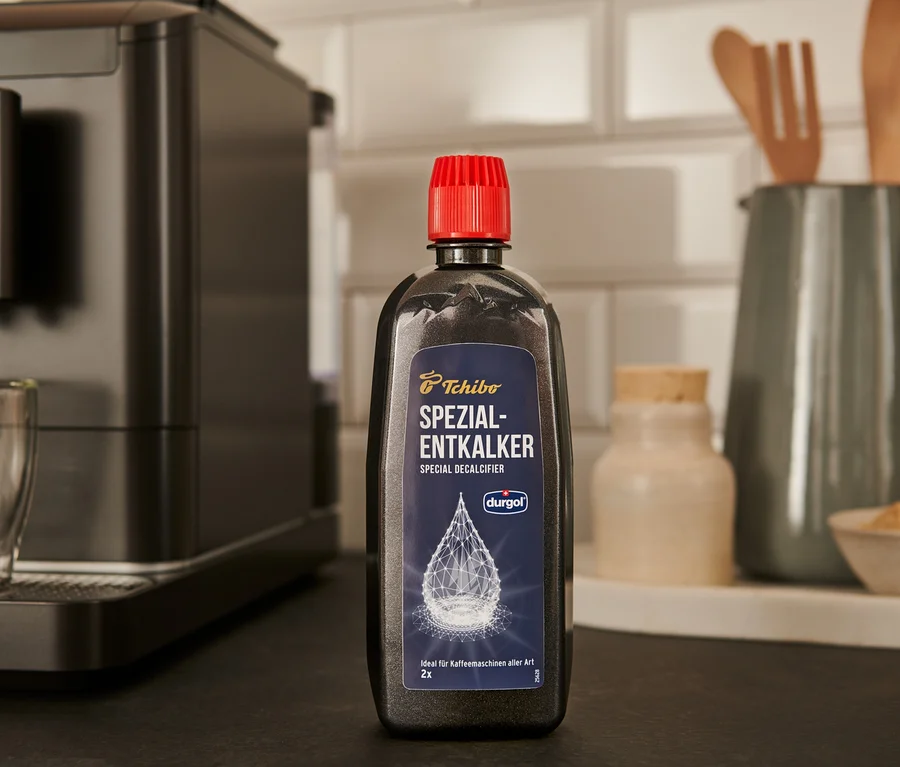 Černá láhev odvápňovače durgol® speciální odvápňovač, 400 ml stojí na lince vedle kávovaru.