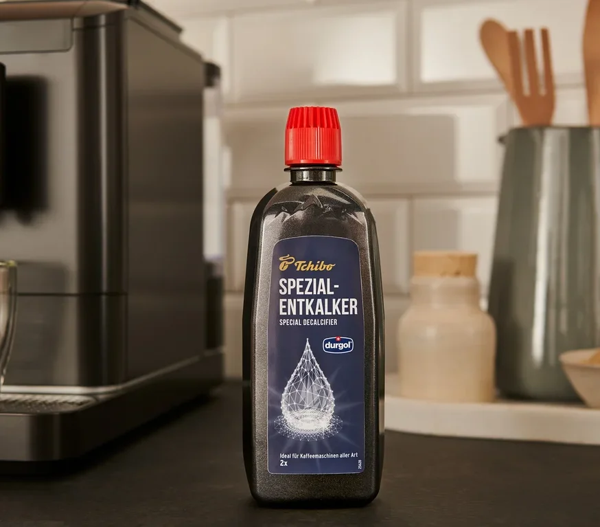 Černá láhev odvápňovače durgol® speciální odvápňovač, 400 ml stojí na lince vedle kávovaru.