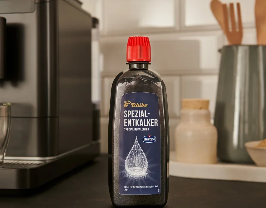 Černá láhev odvápňovače durgol® speciální odvápňovač, 400 ml stojí na lince vedle kávovaru.
