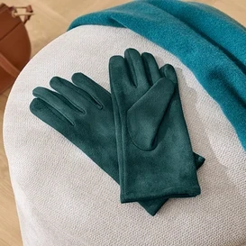 Na bílé stoličce leží zelené rukavice, modrá šála a hnědá kabelka.