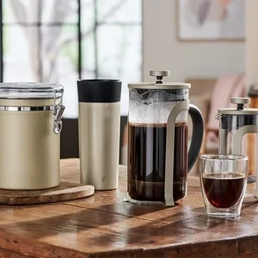 Na dřevěném stole stojí dóza, termoska a french press konvice.