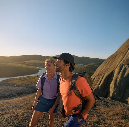 Dva turisté s outdoorovými batohy a oblečením na skalnatém terénu.