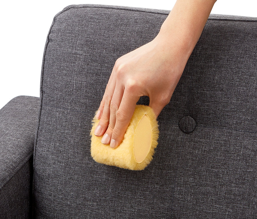 Ruka používá houbičku na skvrny (2 ks) na čištění šedé pohovky.