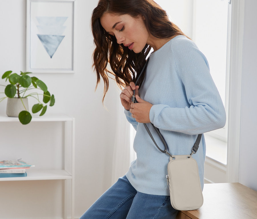 Žena si upravuje popruh mini kabelky krémové barvy.