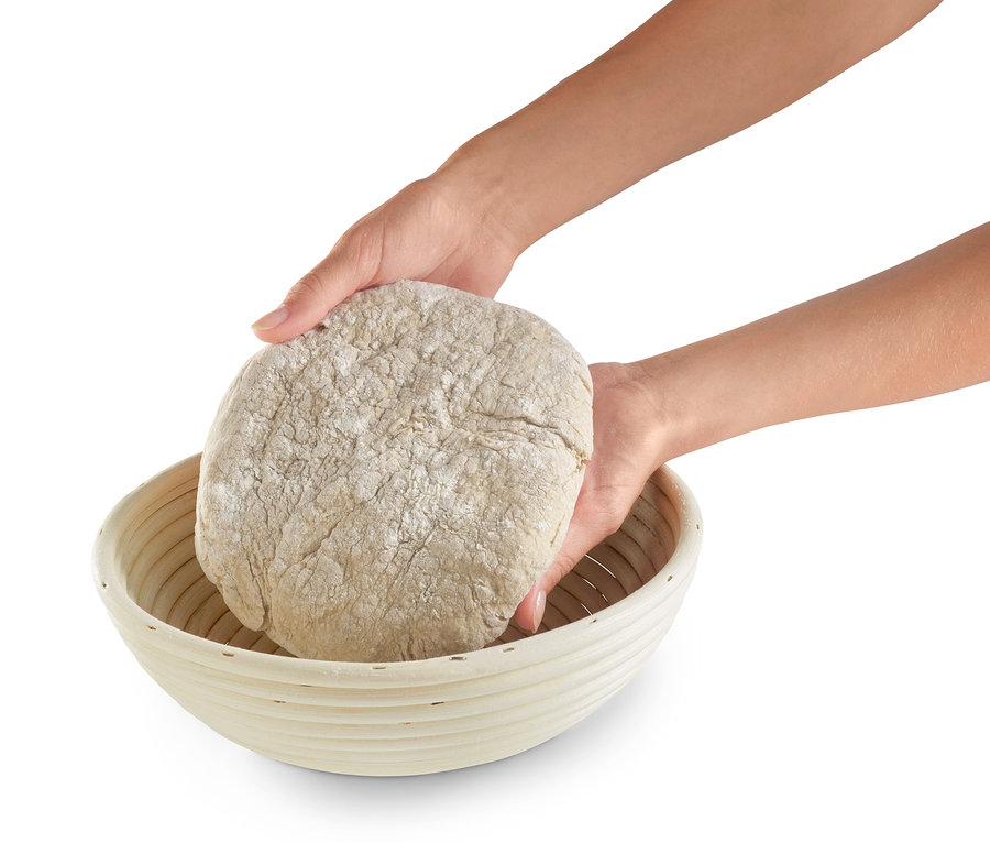 Dvě ruce vkládají bochník těsta do kulaté ošatky na kynutí těsta.