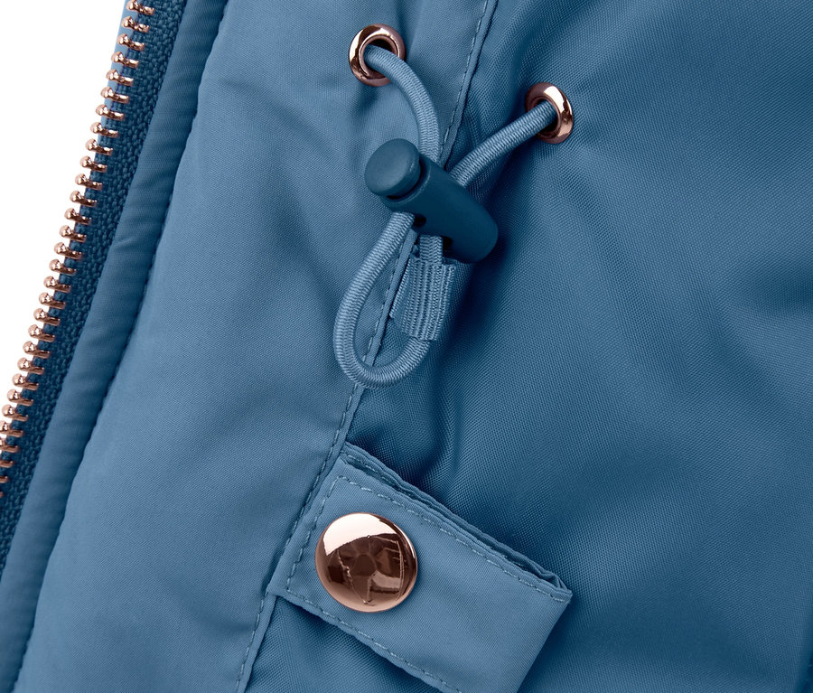 Detail světle modré bundy s bronzovým zipem a stahovací šňůrkou.