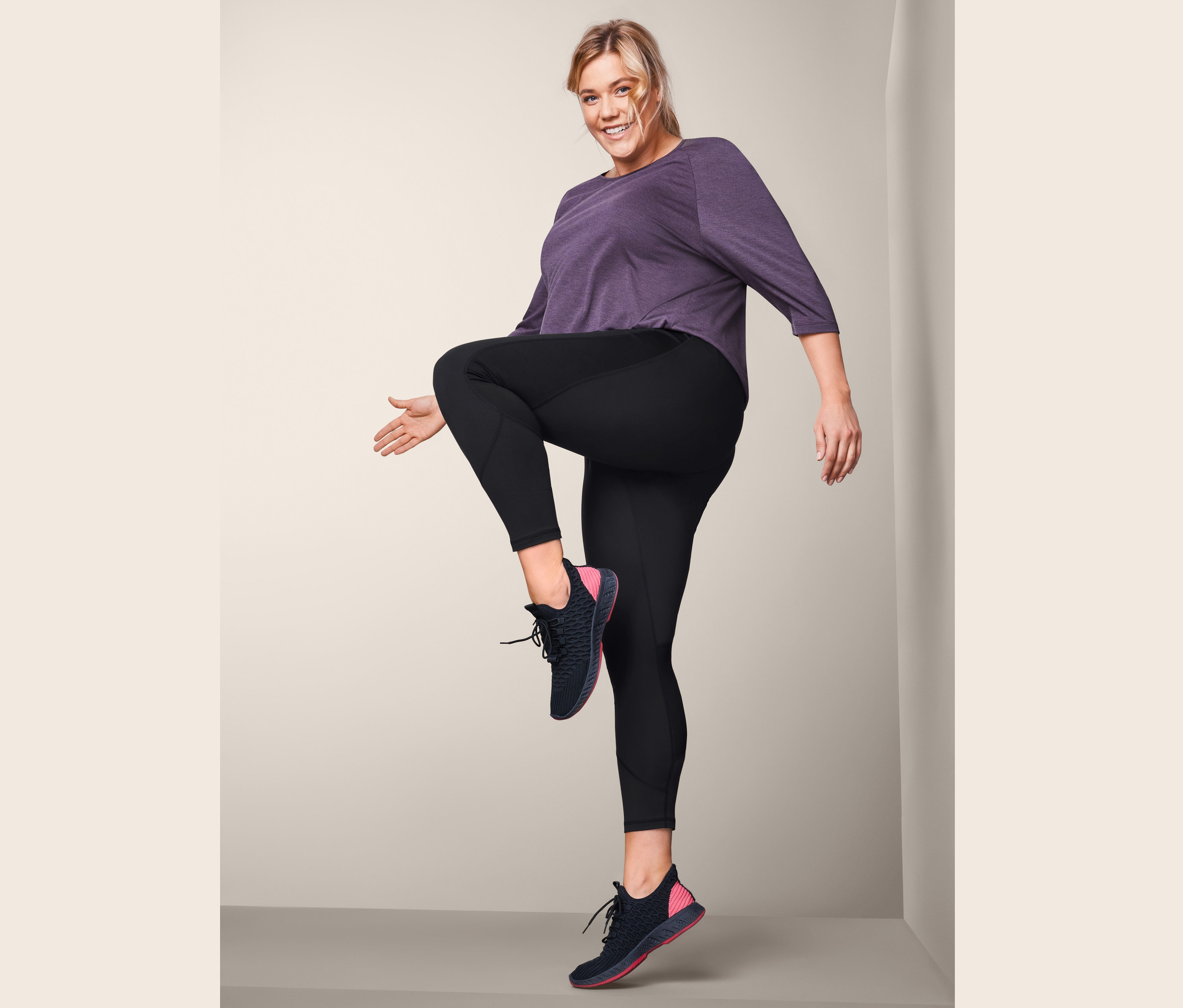 Žena s blond vlasy zvedá koleno v černých sportovních legínách.