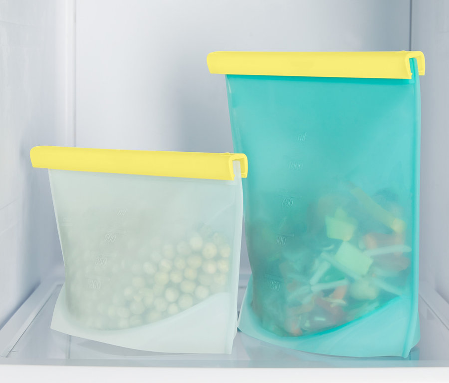 Dva sáčky na potraviny s žlutými uzávěry stojí v chladničce. Jeden sáček je plný hrášku, druhý nakrájené zeleniny.