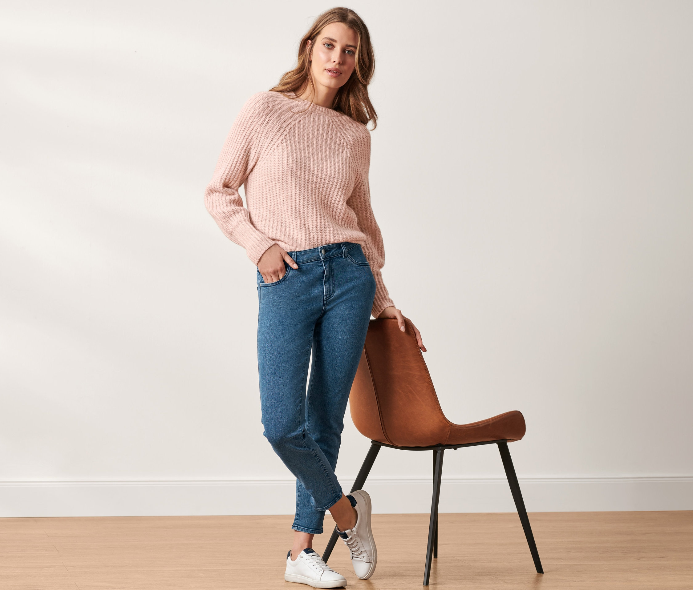 Žena pózuje v růžovém svetru a džínách »Slim Fit«.