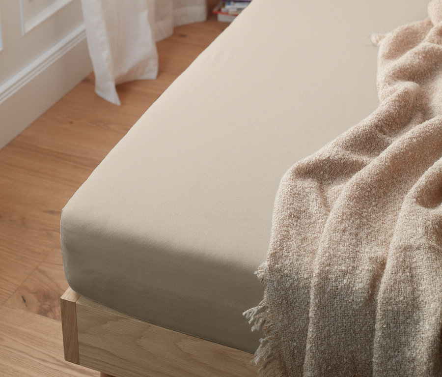 Krémové žerzejové napínací prostěradlo na posteli.