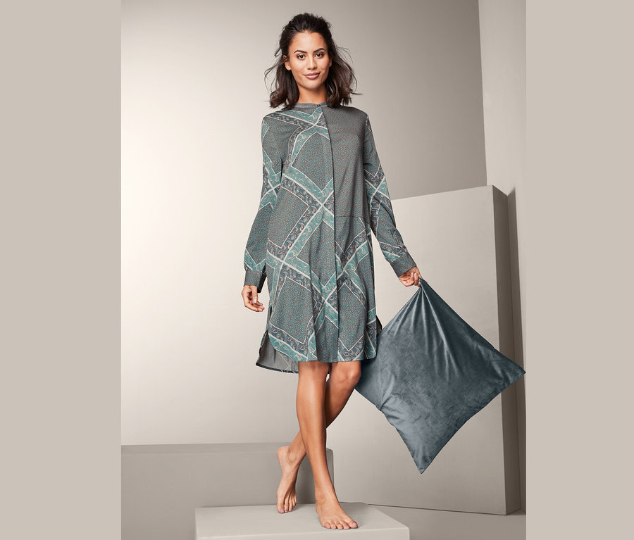 Žena drží šedý polštář a má na sobě noční košili.