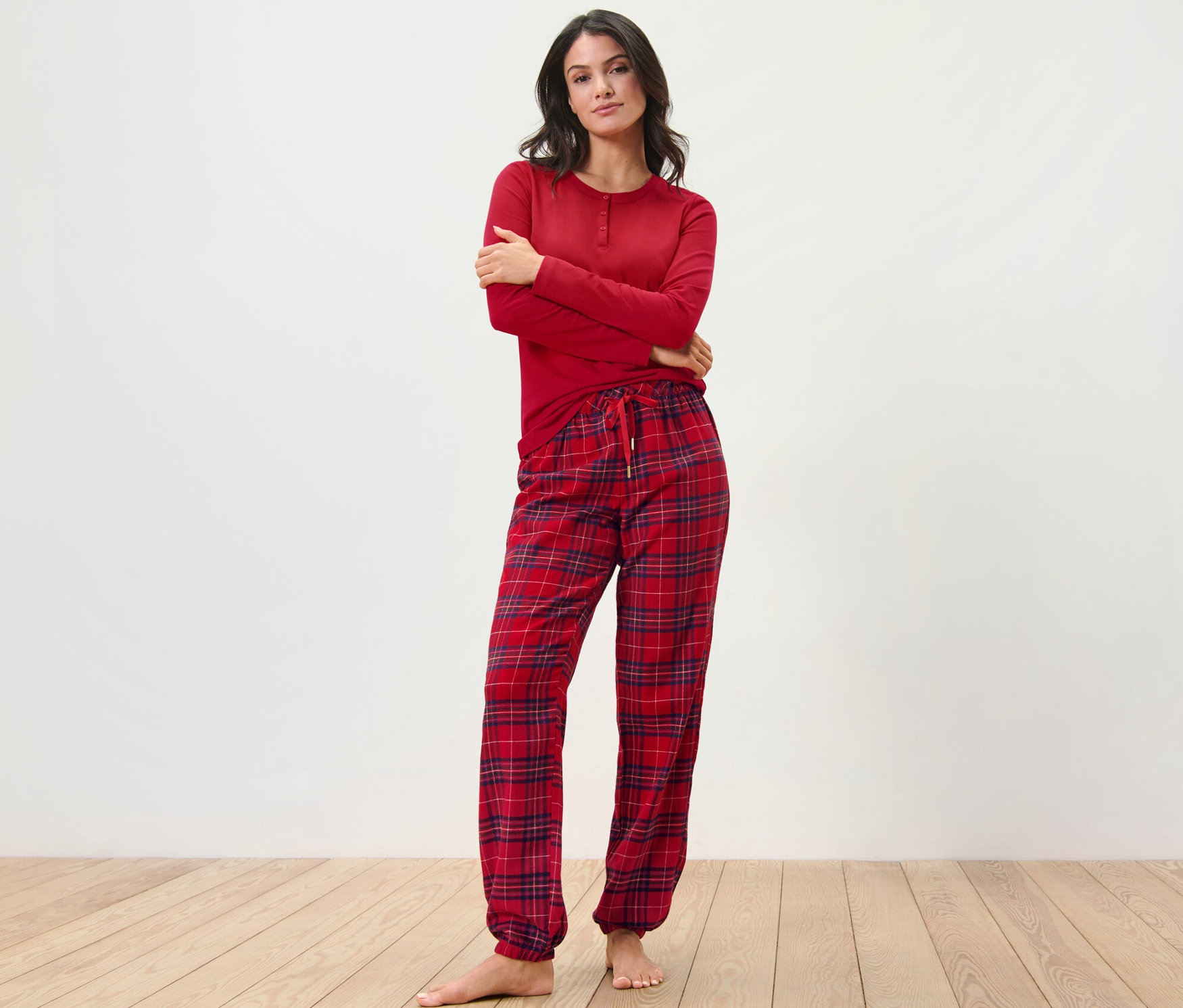 Žena pózuje v červeném flanelovém pyžamu s kostkovaným vzorem.
