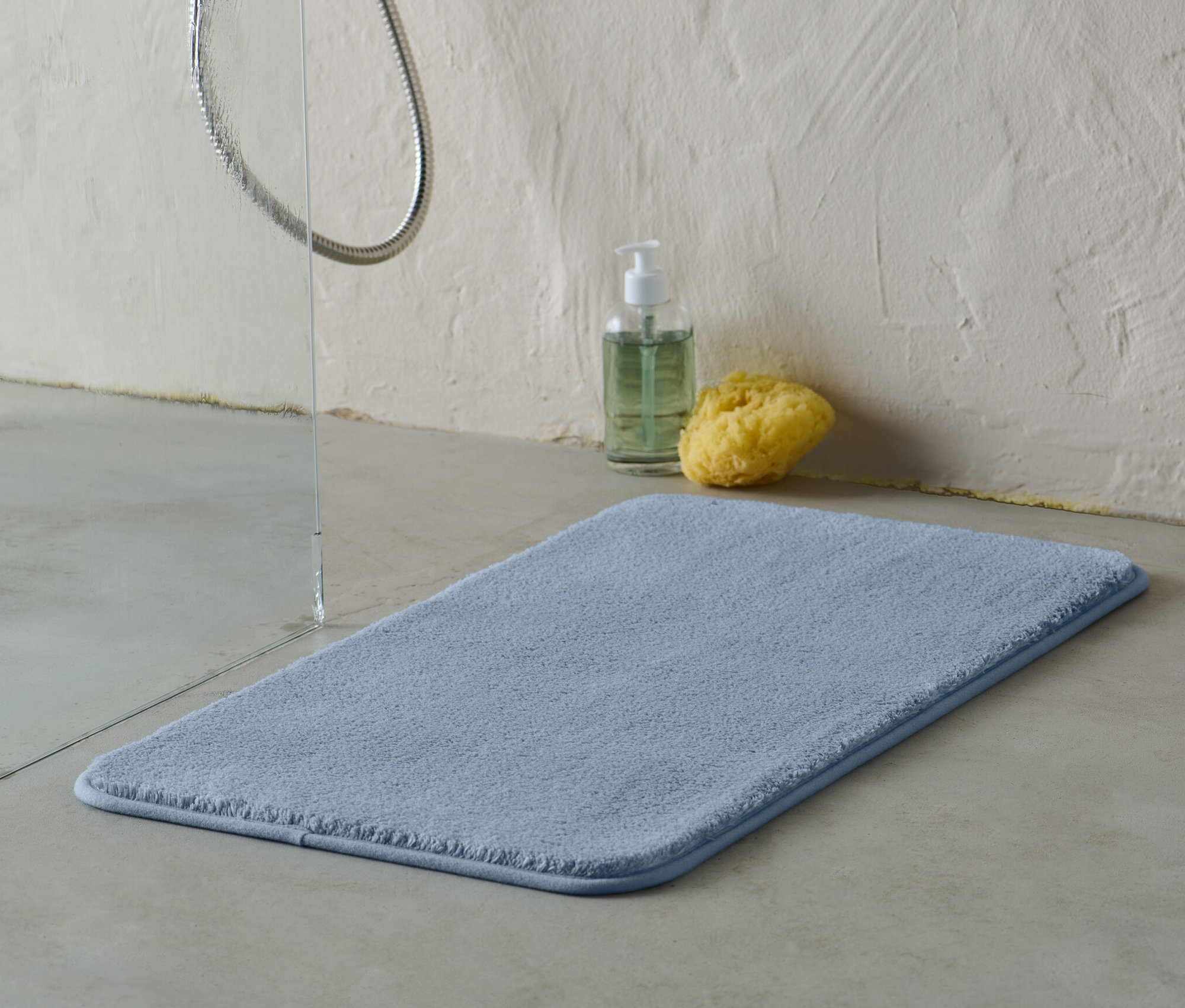 Modrá koupelnová předložka cca 70 x 40 cm leží na podlaze vedle sprchy.