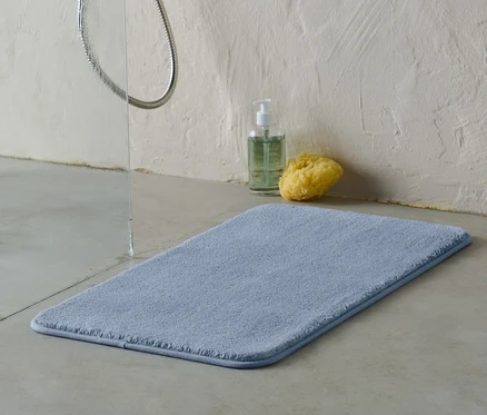 Modrá koupelnová předložka cca 70 x 40 cm leží na podlaze vedle sprchy.
