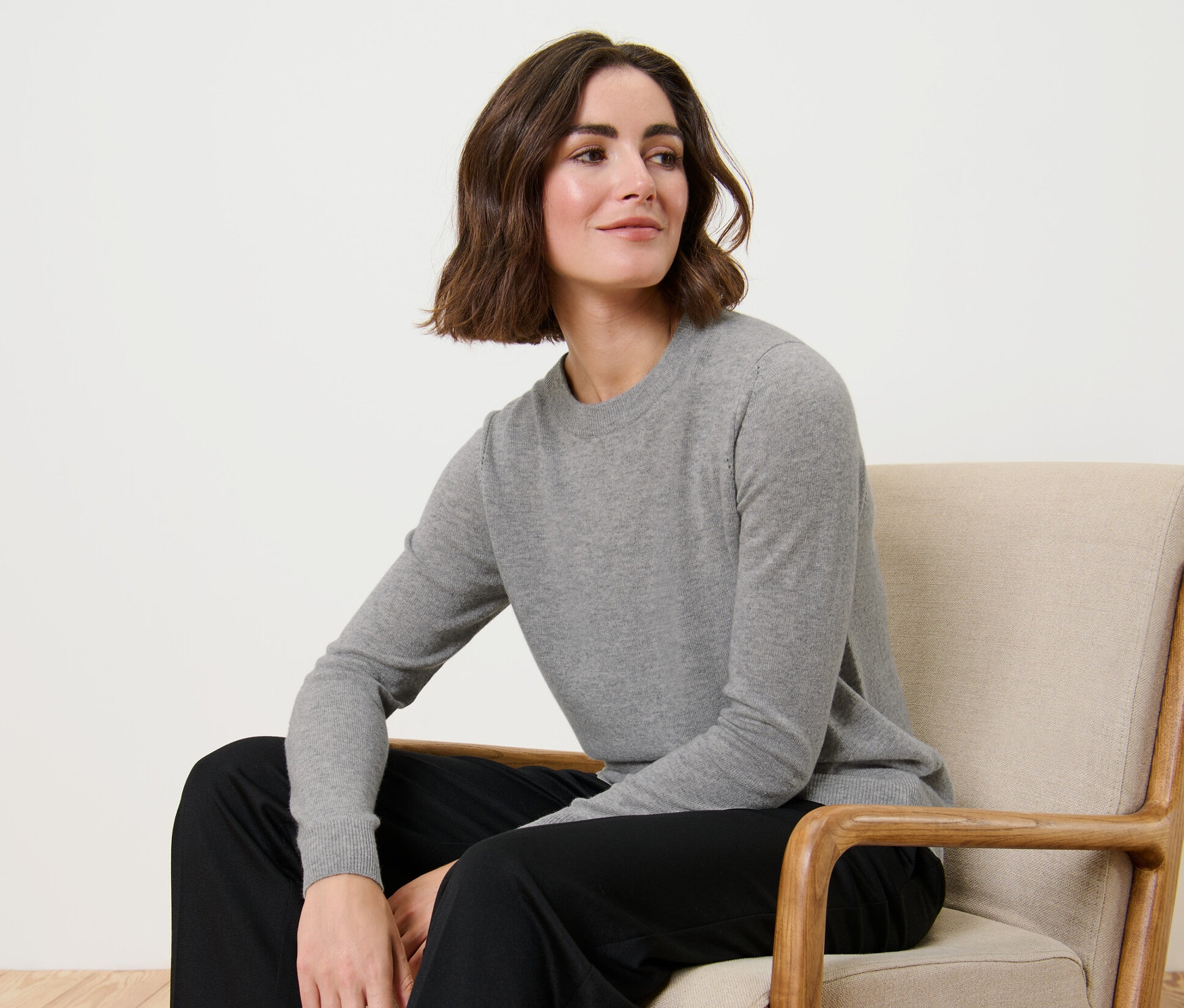 Žena sedí v křesle a má na sobě šedý melírovaný svetr z jemného úpletu s kašmírem.
