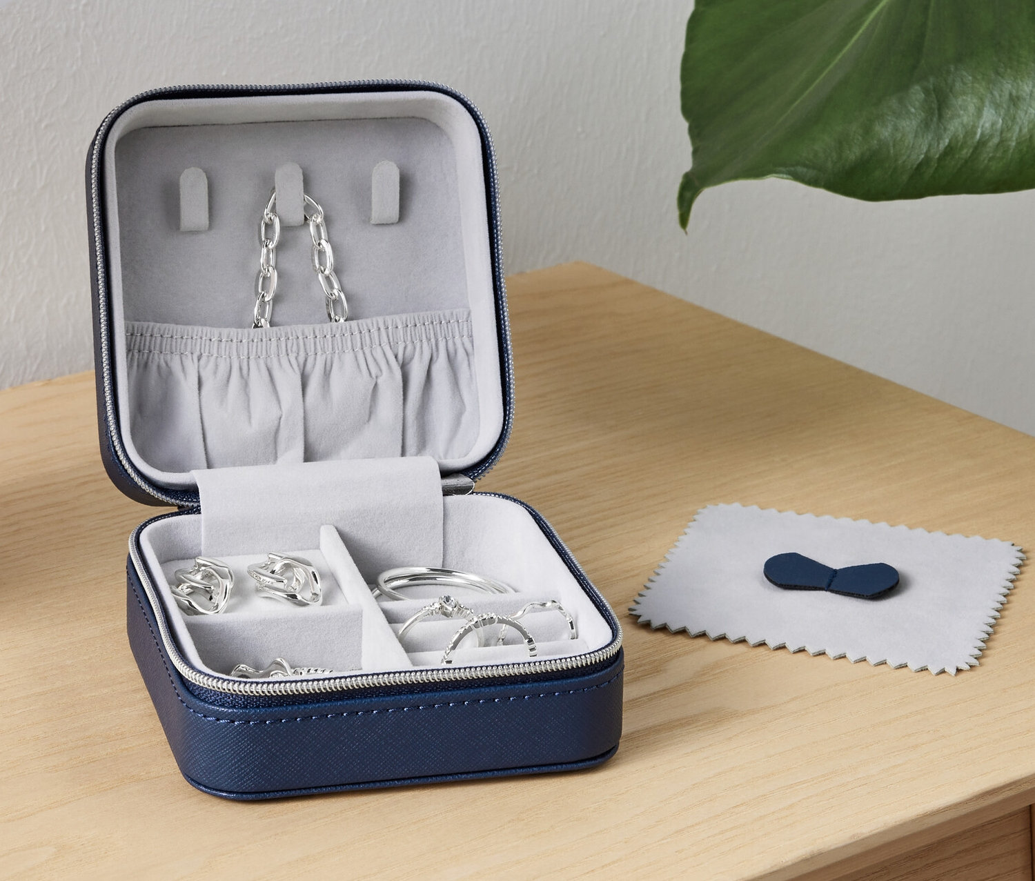 Otevřená malá šperkovnice s šperky uvnitř stojí na stole vedle lampy.