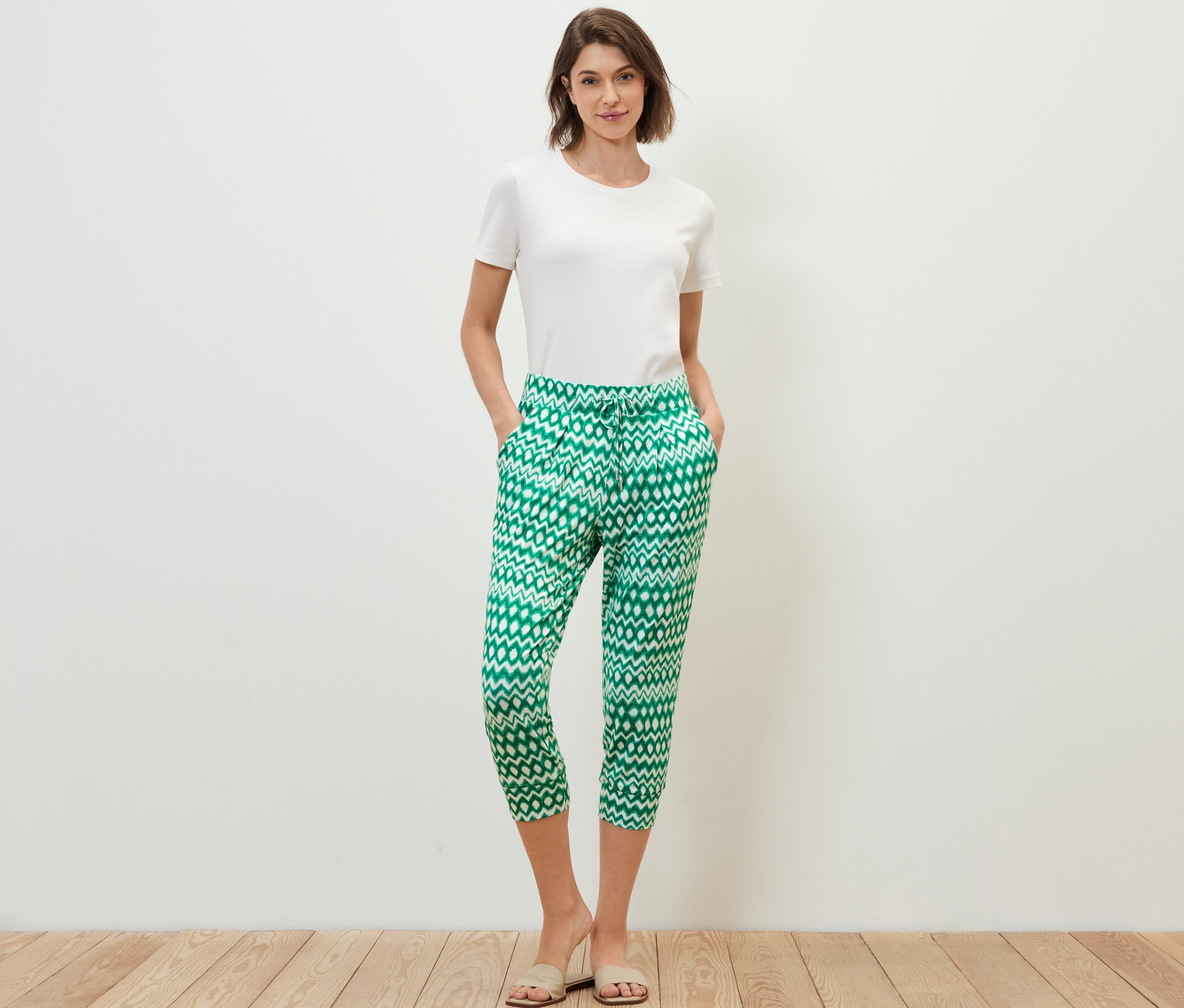 Žena stojí a má ruce v kapsách 3/4 žerzejových kalhot s potiskem.