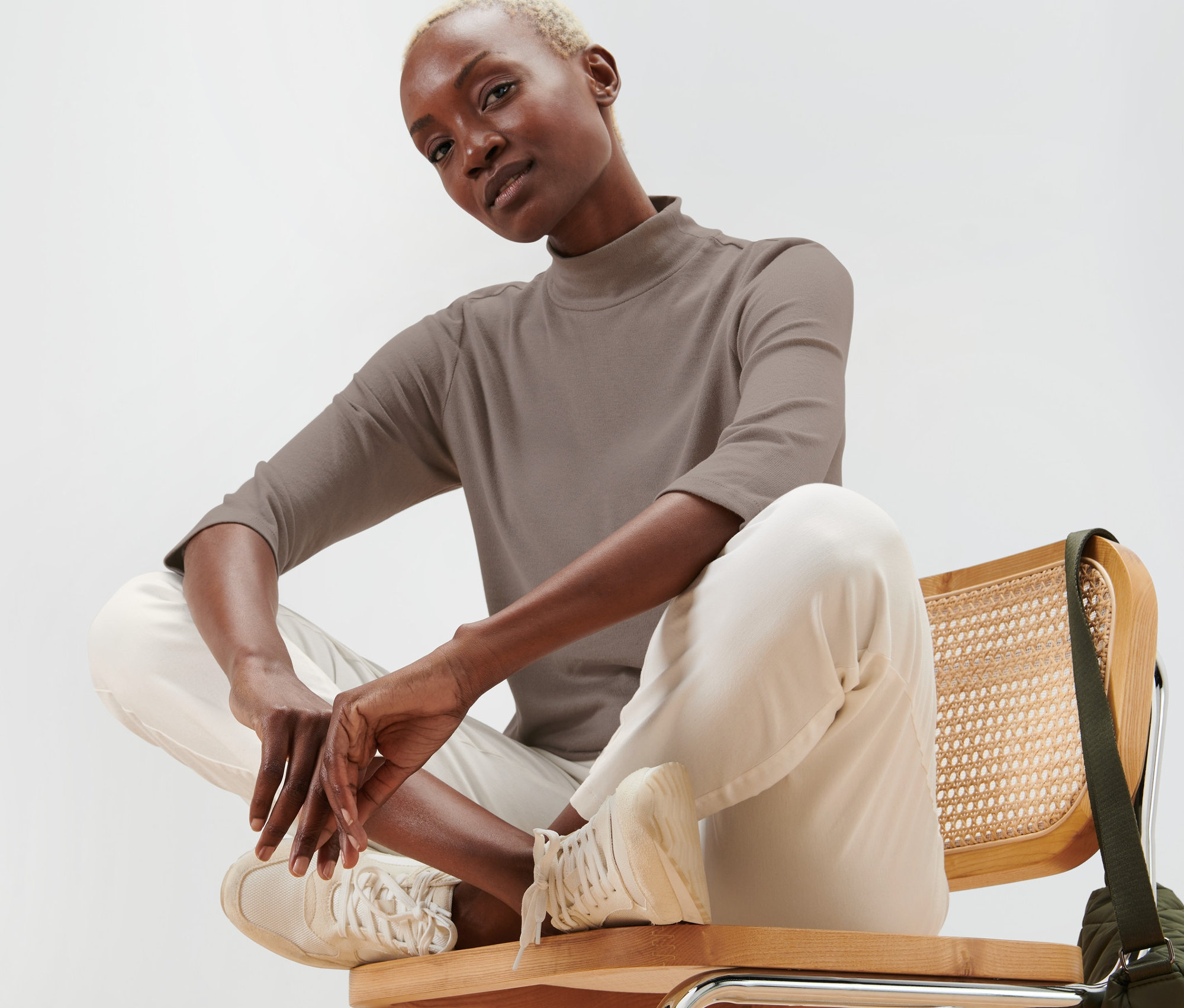 Žena sedí na židli a má na sobě taupe triko z jemného úpletu.