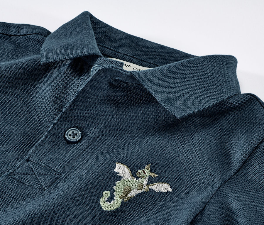 Detail modré dětské polokošile z bavlněného piké s výšivkou draka.