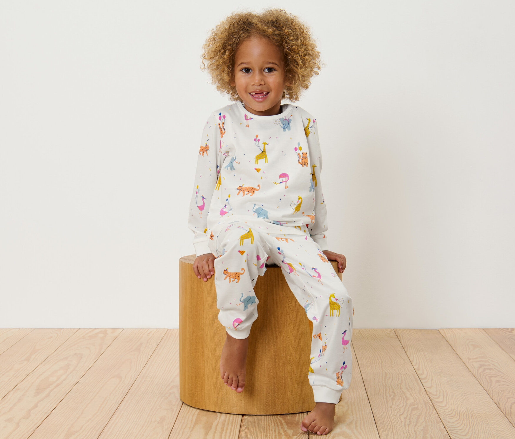 Dítě sedí na dřevěné stoličce a má na sobě dětské pyžamo s potiskem zvířat.