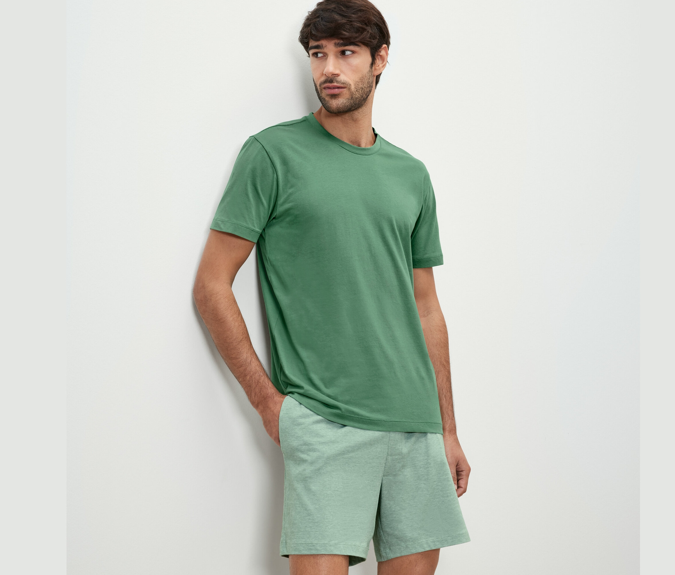 Muž opřený o zeď má na sobě krátký pyžamový set.