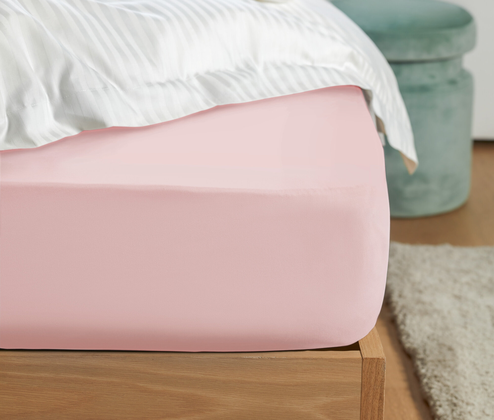 Detail růžového prostěradla na posteli s bílým pruhovaným povlečením a zelenou stoličkou v pozadí.