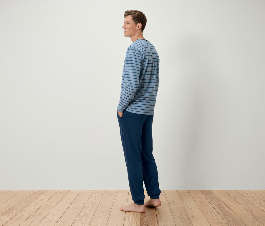 Muž stojí bokem a má na sobě modré pruhované tričko s dlouhým rukávem a tmavě modré kalhoty.