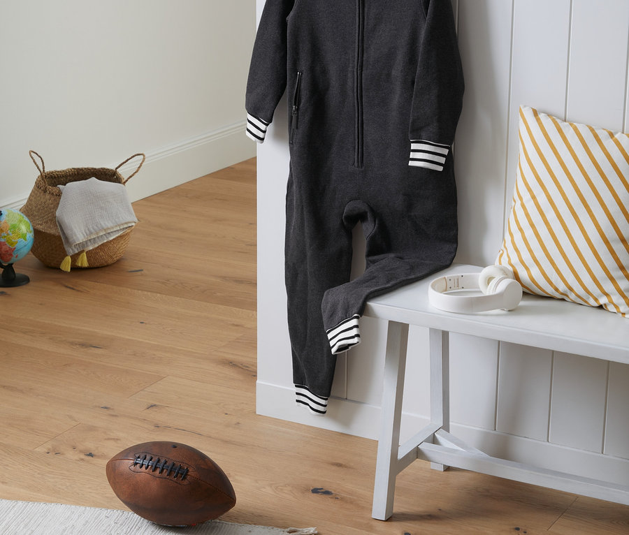 Tmavě šedý dětský overal visí na bílém věšáku vedle bílé lavice.