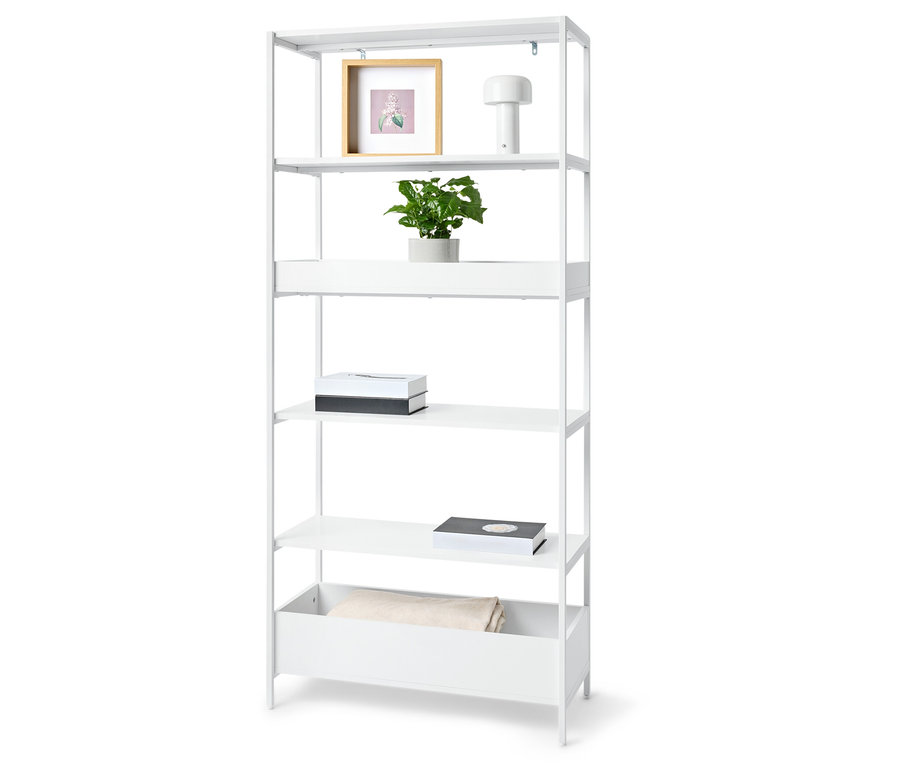 Bílá knihovna s pěti policemi s rostlinou, rámečkem s obrázkem, lampou, dvěma krabicemi a dekou.