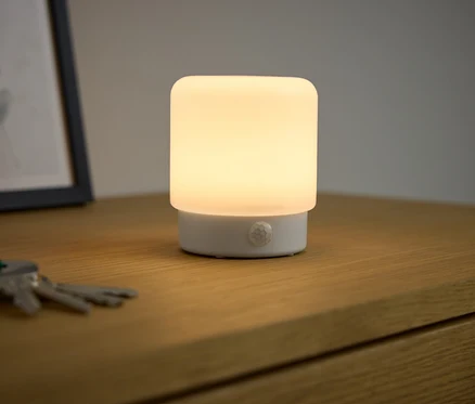 Na dřevěném stolku svítí multifunkční LED lampička s pohybovým senzorem.