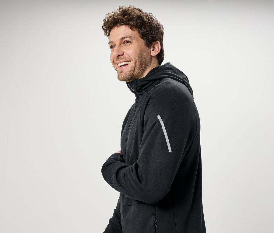 Usmívající se muž s kudrnatými vlasy má na sobě černou mikinu s kapucí.