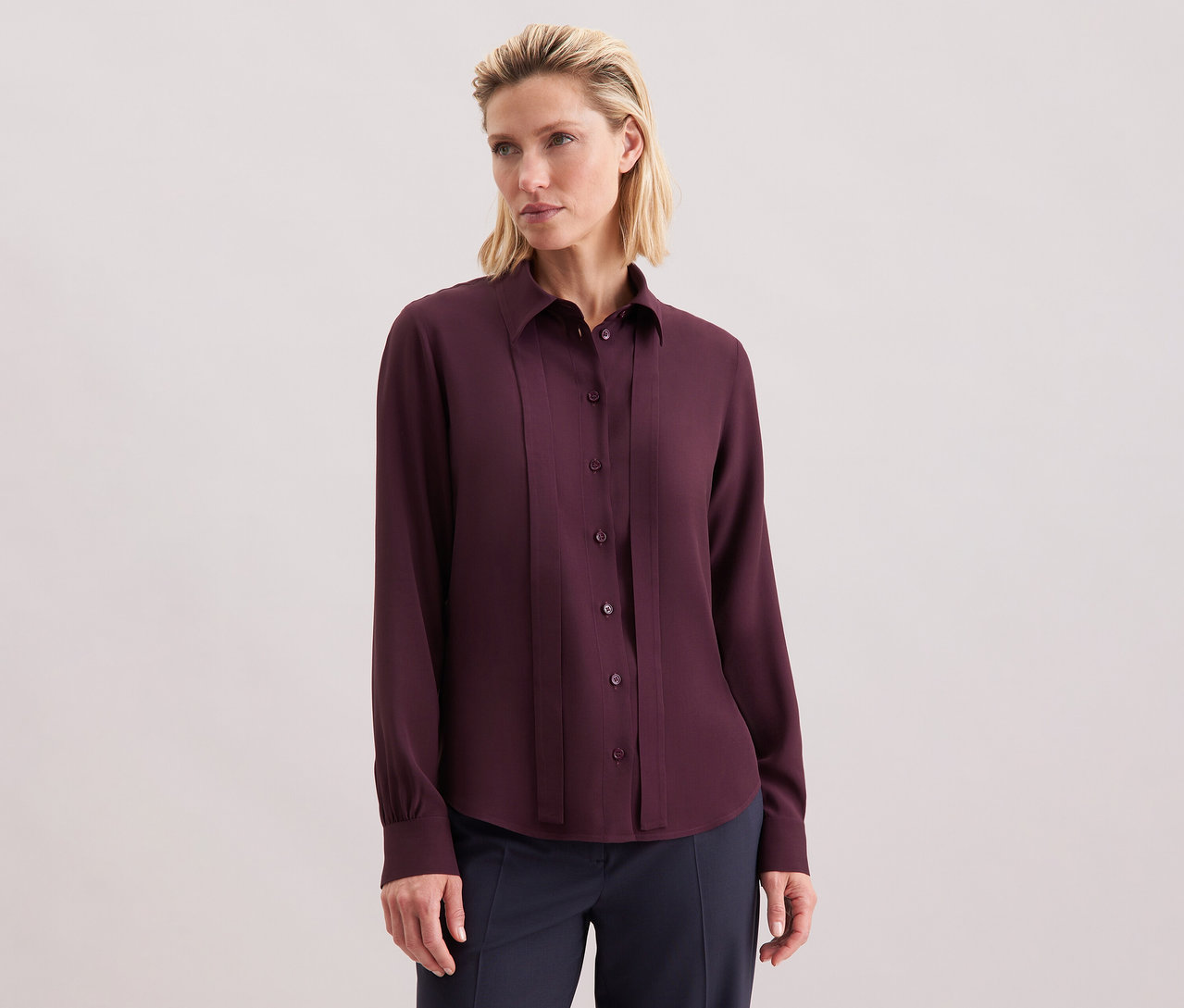 Žena má na sobě viskózovou halenku s vázačkou Seidensticker, bordó, s knoflíky.