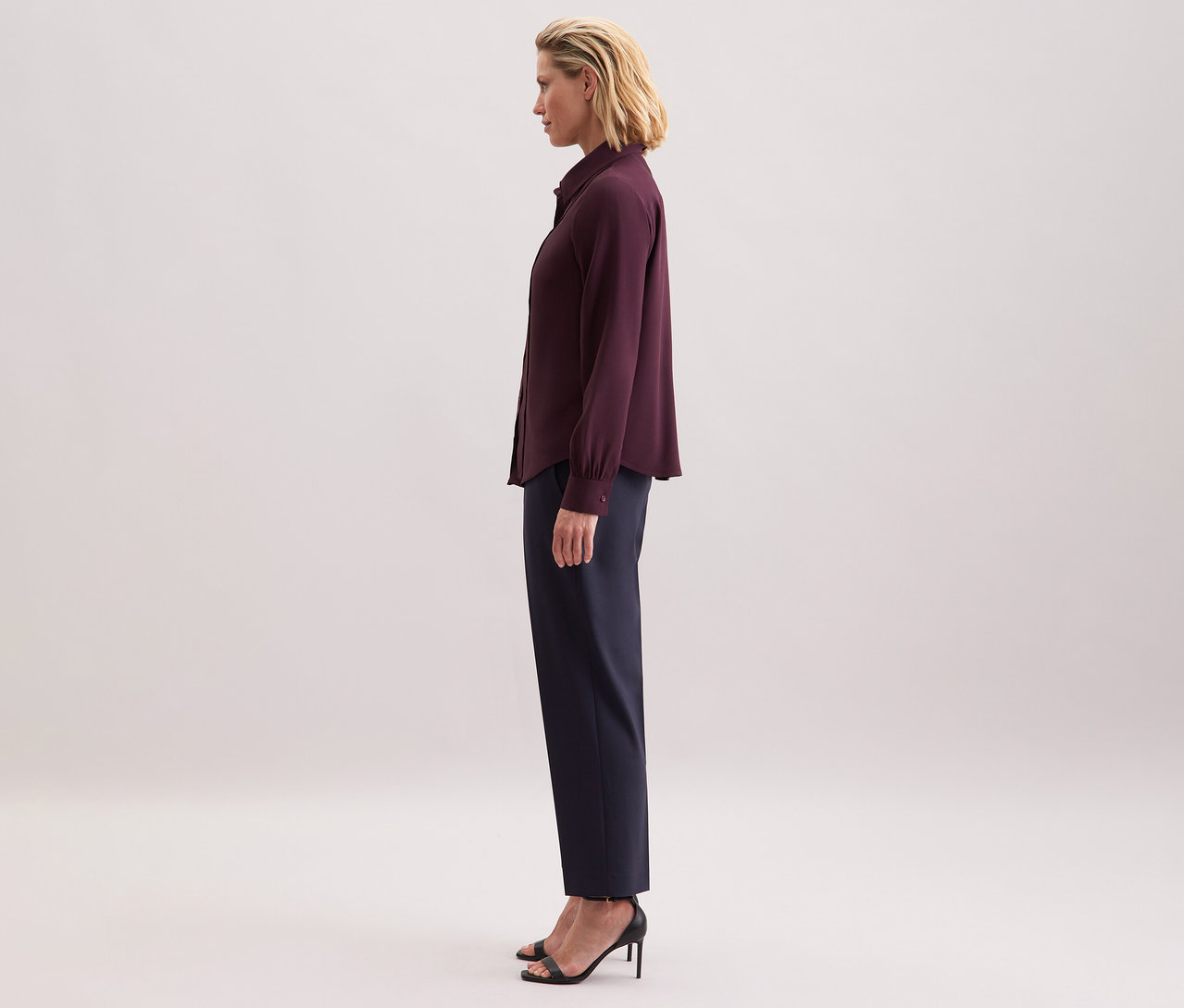 Žena má na sobě viskózovou halenku s vázačkou Seidensticker, tmavé kalhoty a černé sandály.