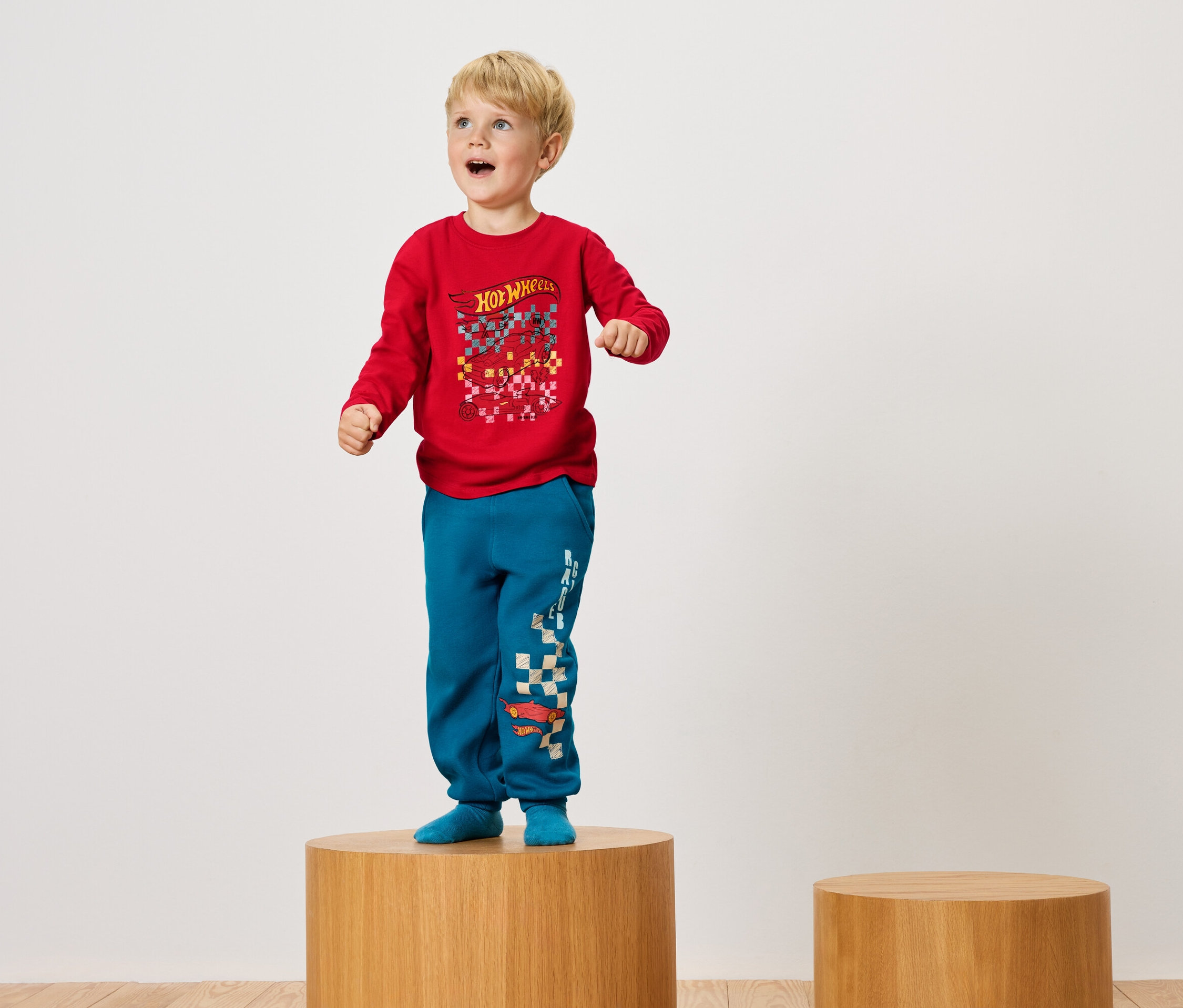 Chlapec stojí na dřevěném podstavci v červeném tričku a modrých kalhotách.