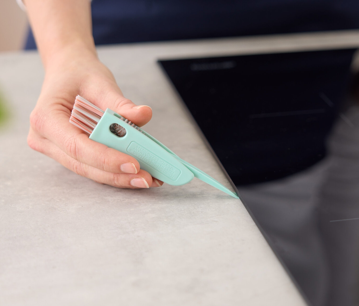 Žena čistí okraj varné desky čisticím kartáčkem 3 v 1.