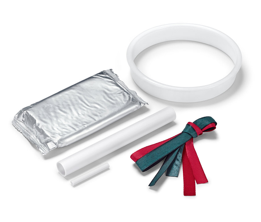 Balíček v stříbrném obalu, bílý kruh, dvě bílé tyčinky a červeno-zelená stuha na bílém pozadí.