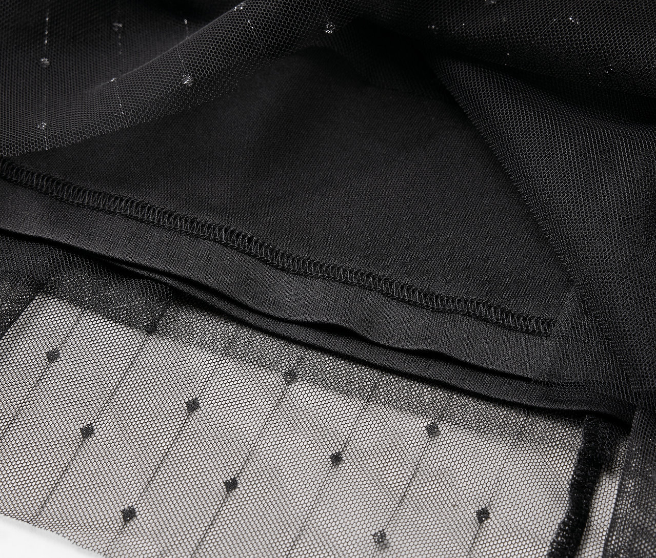 Detail černého tylového oděvu s tečkovaným vzorem a vnitřní podšívkou.