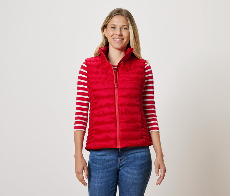 Žena má na sobě červenou prošívanou vestu, proužkované tričko a džíny.