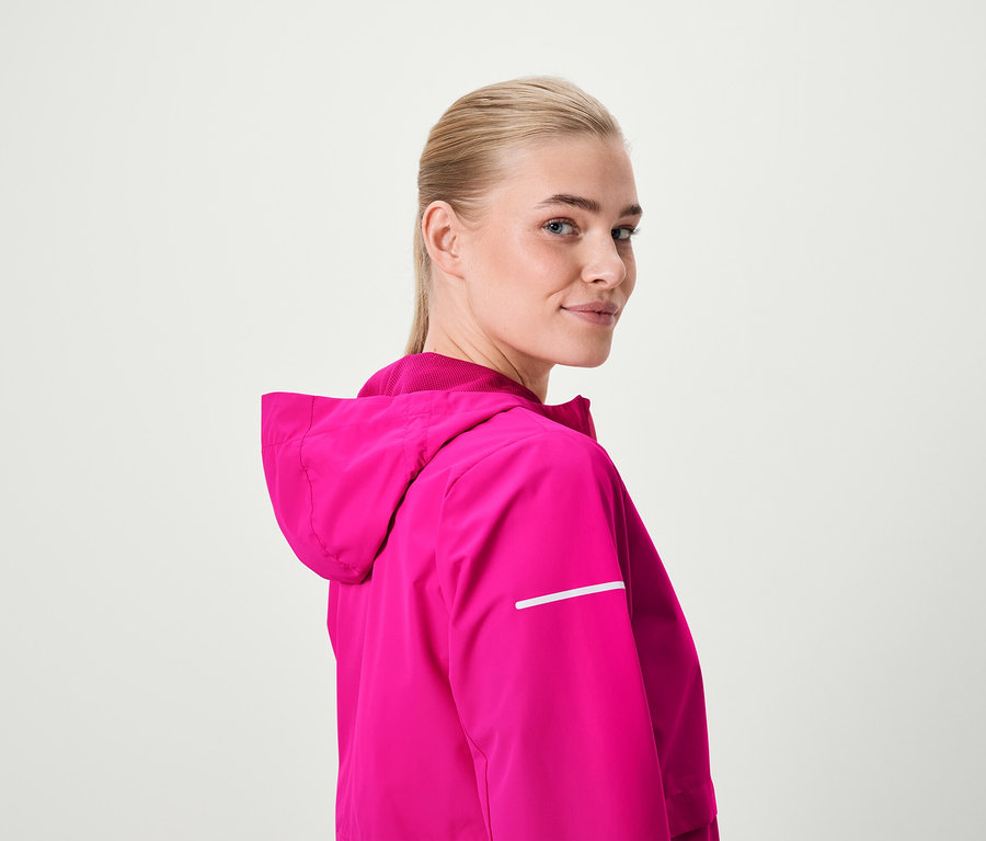 Blondýna se dívá přes rameno a má na sobě růžovou bundu s kapucí.