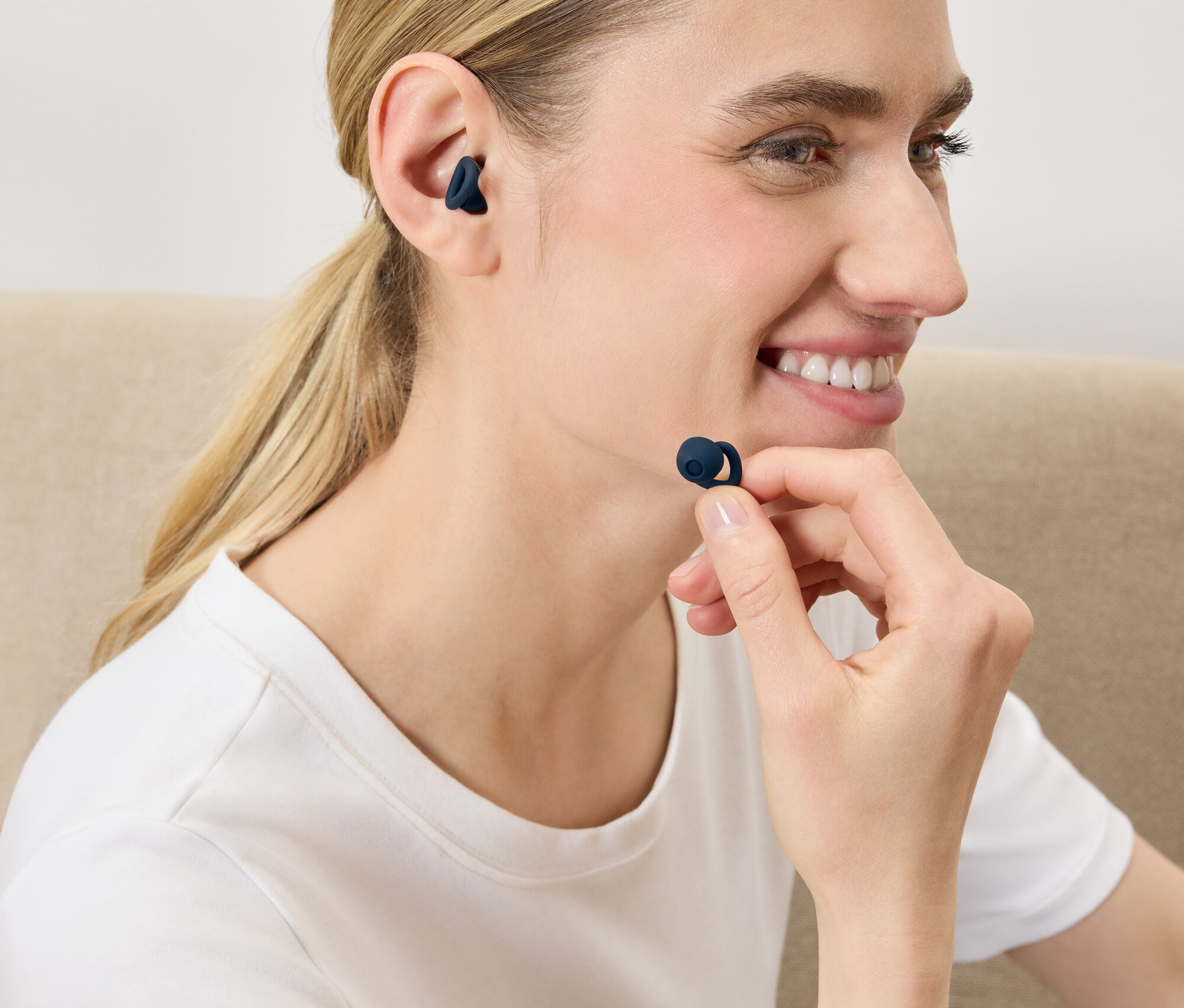 Žena si vkládá do ucha tmavě modré bezdrátové sluchátko.