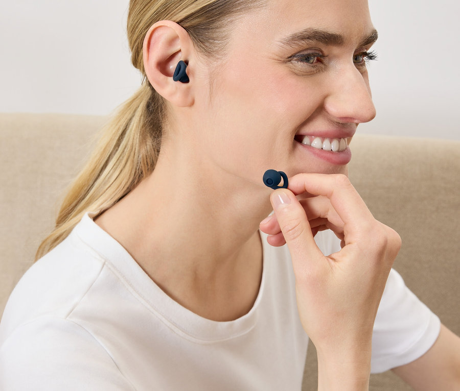 Žena si vkládá do ucha tmavě modré bezdrátové sluchátko.