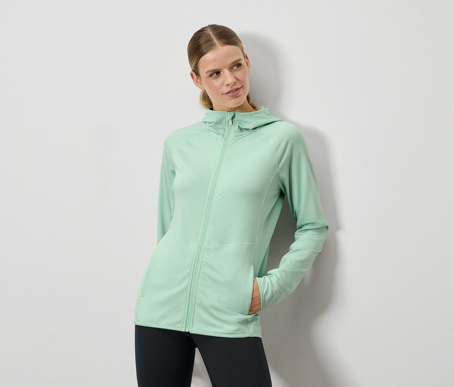 Žena pózuje v mátově zelném svetru s kapucí a černých legínách.