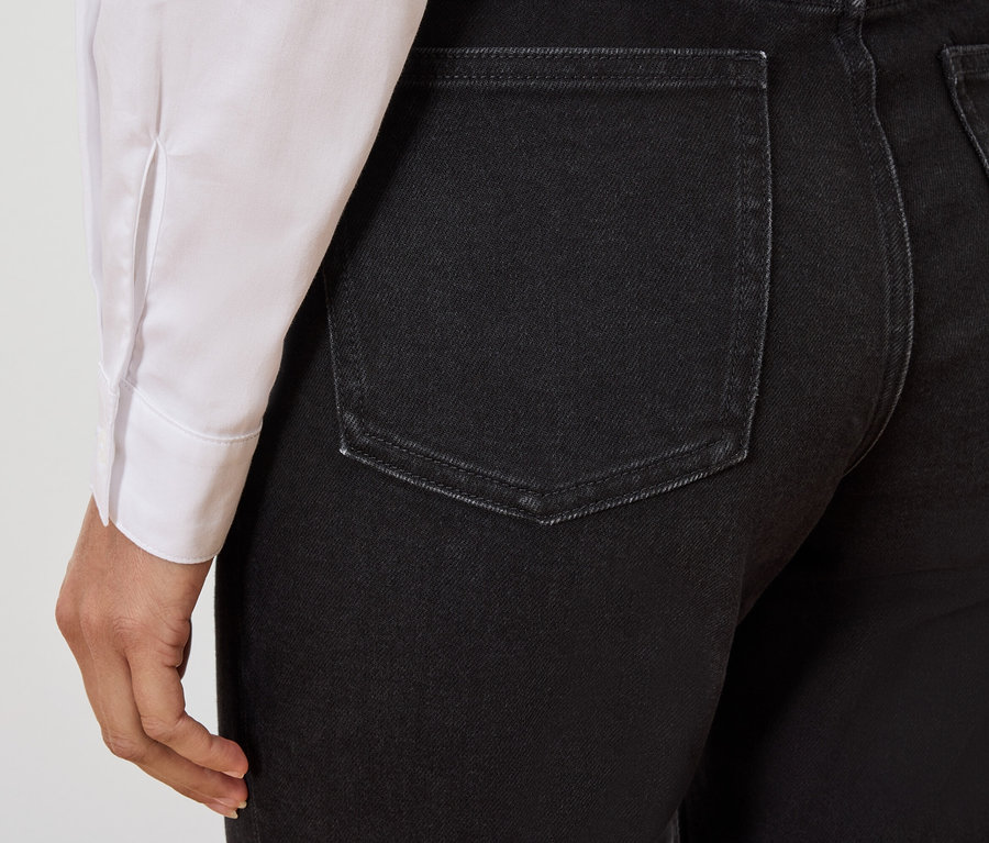 Detail zadní části černých džínů na osobě, která má na sobě bílou košili.